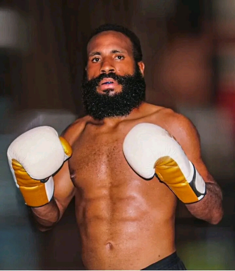 Bearded PNG fighter with gold and white boxing gloves raised